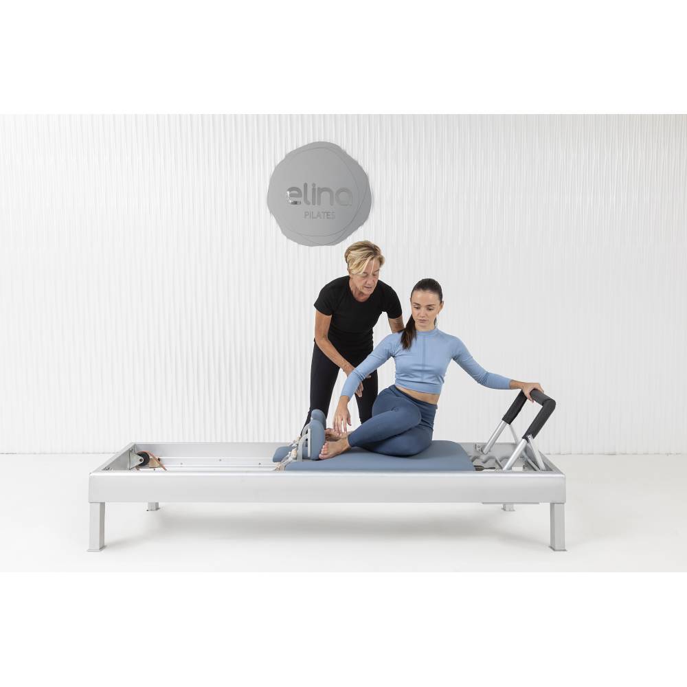 Elina Pilates Classic Aluminum Reformer blue upholstery model with instructor side pose